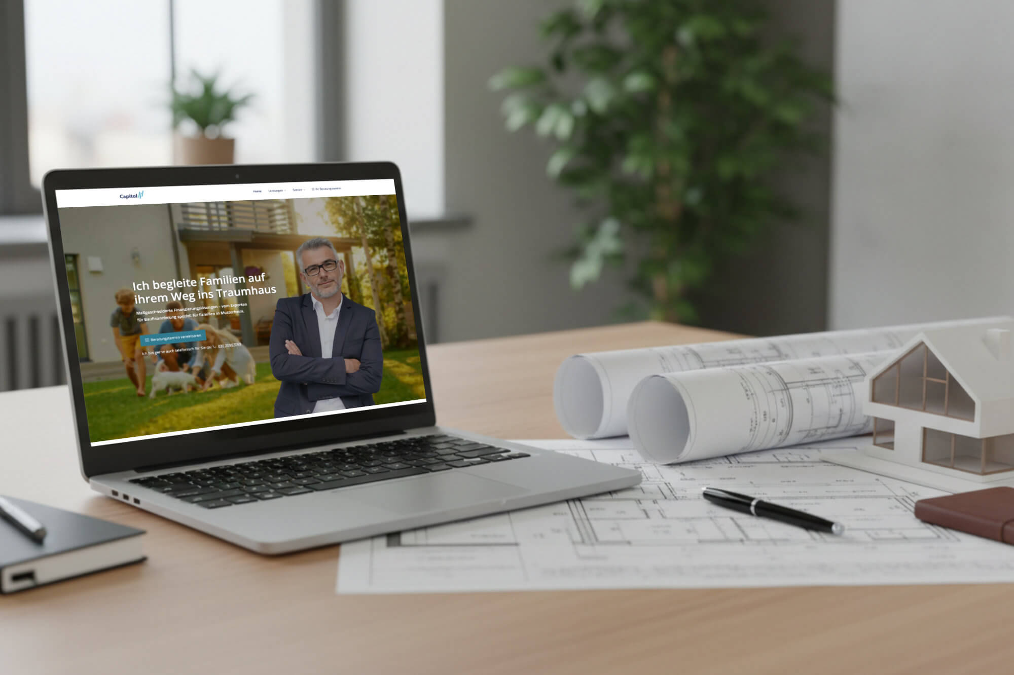 Laptop auf einem Schreibtisch mit Bauplänen, Stift, aufgerollten Zeichnungen und Hausmodell; auf dem Bildschirm eine Website eines Baufinanzierers erstellt.