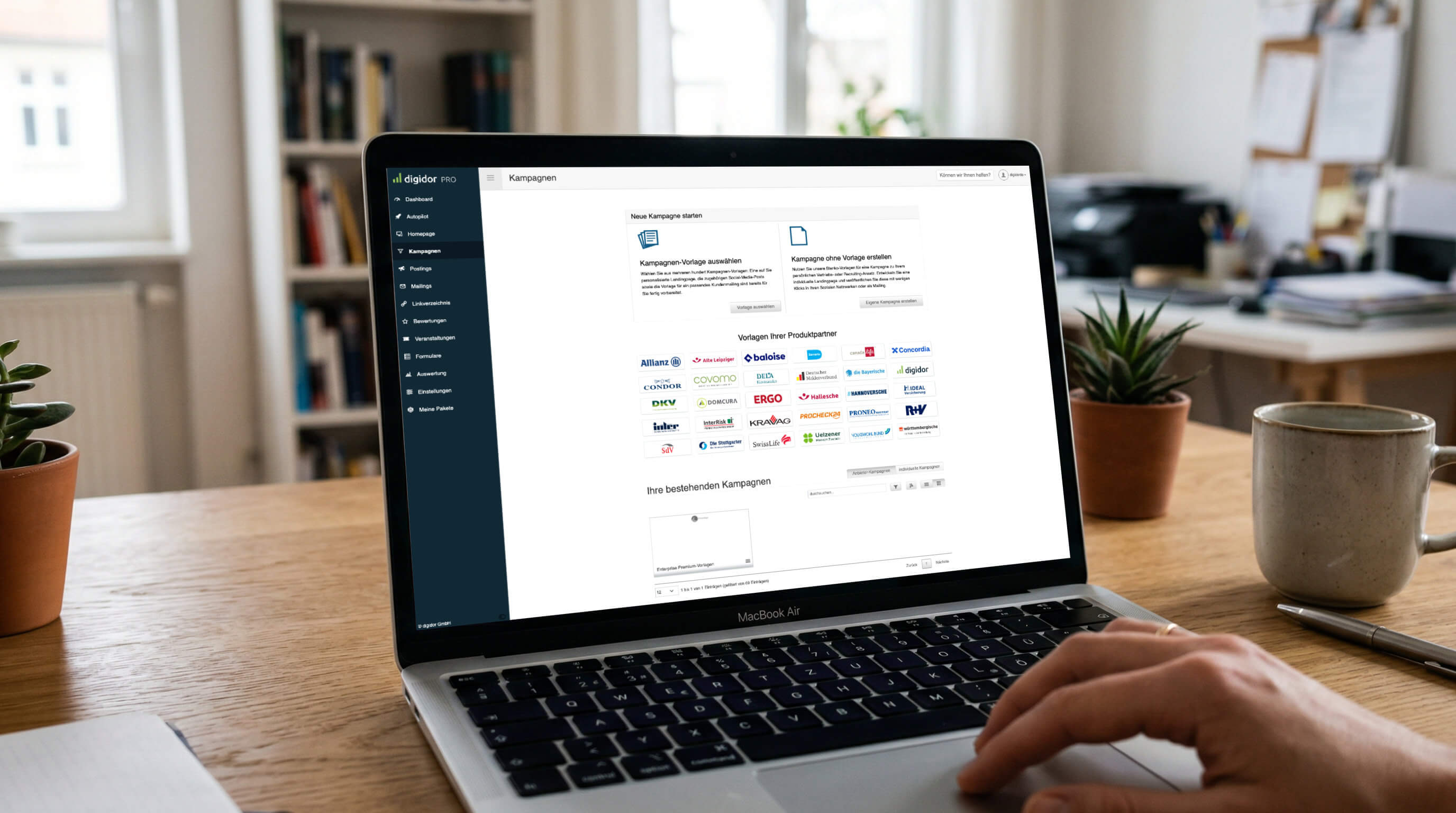 Produktpartner Hand bedient ein Laptop mit geöffneter Weboberfläche auf einem Schreibtisch neben Pflanze und Kaffeetasse.